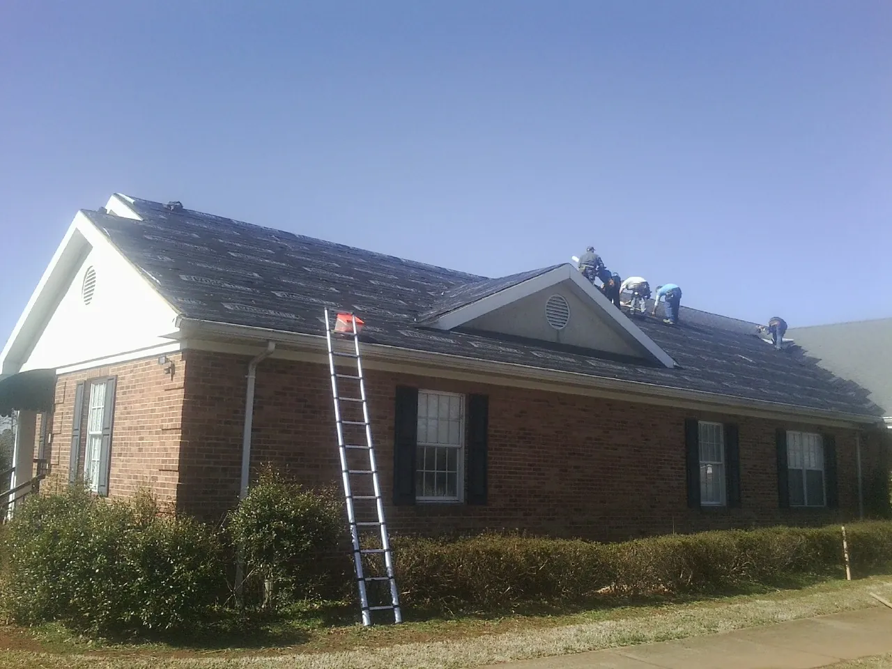 Crew tearing shingles off a brick ranch roof with a ladder set — Emergency Roof Repair work by our crew in Mohnton