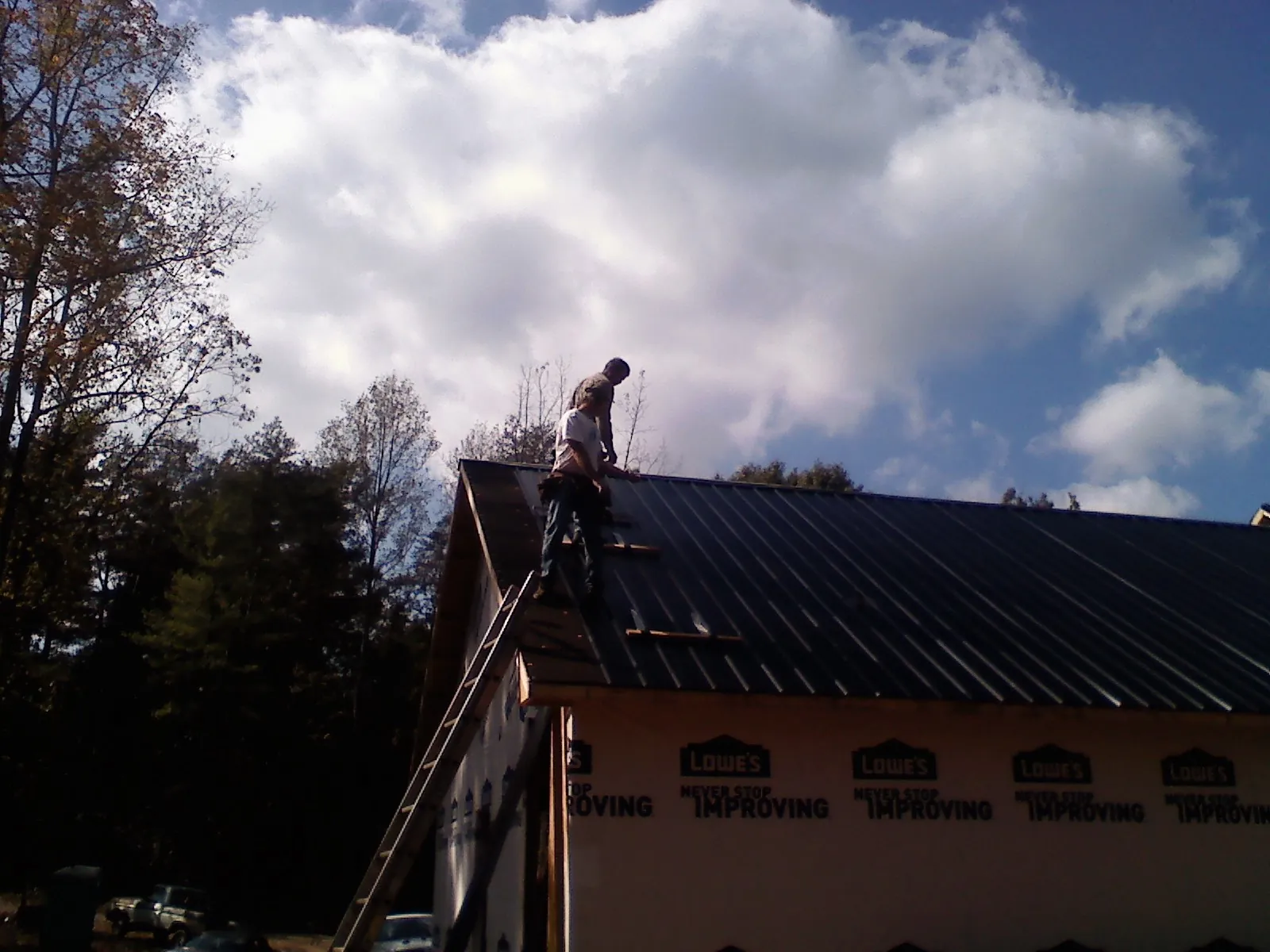 Roofer fastening dark metal panels high against a cloudy sky, from a Roof Inspection job in Mohnton