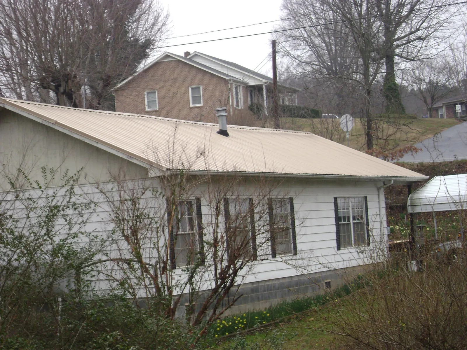 Tan metal roof on a white sided house set into a hillside — Commercial Roofing by Roofing Brothers in Mohnton